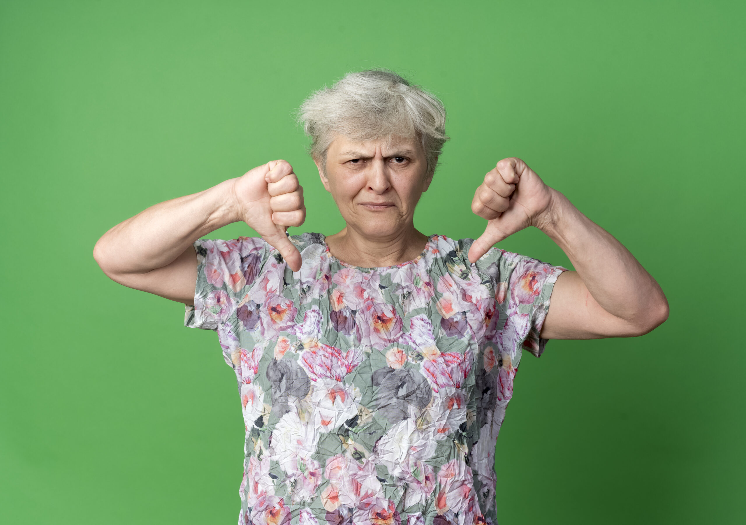 Displeased Elderly Woman Thumbs Down With Two Hands Isolated On Green Background With Copy Space